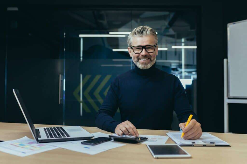 Portrait of an older gray-haired man, an accountant, an auditor sitting in the office at a laptop